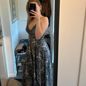 Svart och grå långklänning med paisleymönster - Säljer en långklänning med djup v-ringning och breda axelband. Klänningen har ett svart och grått paisleymönster och är i ett lätt, flödande material. Perfekt för sommardagar eller när du vill känna dig extra fin.