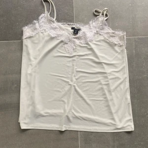 Vit linnetopp med spetsdetaljer - Säljer en vit linnetopp från amisu med tunna axelband och vacker spets upptill. Perfekt att styla till jeans eller kjol för en fräsch look.