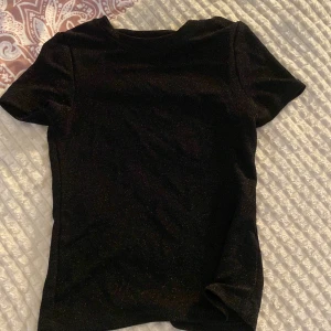 Svart glittrig topp med kort ärm - Snygg svart topp med glittrigt tyg och korta ärmar. Storlek 146-152 men passar som xs. 