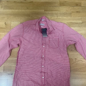 Rutig röd skjorta från Trust XXL - Snygg röd och vit rutig skjorta från Trust i storlek XXL. Skjortan har klassisk krage, bröstficka och vita knappar framtill. Perfekt för dig som gillar en tidlös och stilren look. Tillverkad i mjuk bomull som känns skön mot huden.