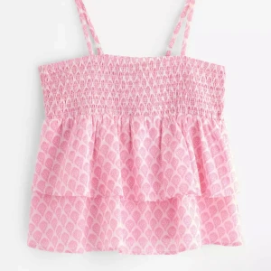 Rosa volangig linnetopp med mönster ALDRIG ANVÄNT! - Supersöt rosa linnetopp med smala axelband och två volanger. Toppen har ett diskret vitt mönster och smockad överdel som ger en skön passform. Perfekt för varma dagar och enkel att matcha med shorts eller kjol.