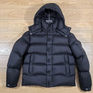  Moncler Vezere - Säljer en svart Moncler dunjacka med avtagbar huva och stora fickor framtill. Jackan har puffig design, lång ärm och klassisk Moncler-logga på ärmen. Perfekt för kalla dagar och riktigt snygg till streetwear-stilen.