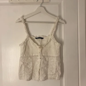 Topp från Zara - Supersöt populär topp från Zara med broderade blommor och spetsdetaljer. Den har knappar framtill och volangkant runt axelbanden. Storlek XS. Använd en gång💗