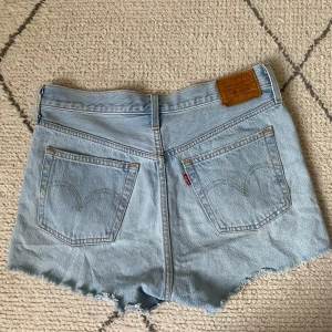Levi's ljusblå jeansshorts med fransar - Ljusblå jeansshorts från Levi's med klassisk femficksdesign, råa fransiga benslut och hög midja.⭐️💕 Ikonisk läderpatch bak och snyggt slitna detaljer framtill. Perfekta för en chill sommardag eller festival.⭐️🫶🏻 Sitter snyggt och har en avslappnad passform. Tyvärr är de för stora för mig, det är därför jag säljer dem💕💕