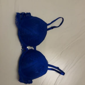 Blå spets-bh från New Yorker 75C - Snygg blå bh från New Yorker i storlek 75C med spetsdetaljer och liten rosett framtill. Bh:n har vadderade kupor, justerbara axelband och fina metalländar på rosetten. Perfekt för dig som gillar färg och detaljer! Säljer då den är för tajt runt om, knappt använd. 