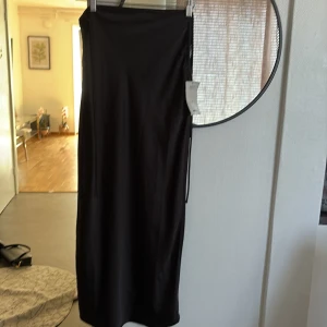 Svart långkjol från MOTF Shein - Stilren svart långkjol från MOTF med slät, glansig yta och rak passform. Kjolen har en enkel design utan mönster och är tillverkad i ett satinliknande material som ger en lyxig känsla. Perfekt för dig som gillar minimalistisk och chic stil.