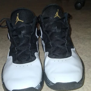 Nike Air Jordan 1 svart/vit/guld US11 - Säljer ett par Nike Air Jordan 1 i svart och vitt med snygga gulddetaljer på tungan och hälen. Skorna har klassisk snörning, rund tå och är tillverkade i en mix av skinn och textil. Perfekta för dig som vill sticka ut med en ikonisk sneaker.