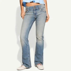 Ljusblå bootcut jeans med dubbla knappar - Snygga ljusblå jeans med bootcut passform och dubbla knappar i midjan. Jeansen har klassisk femficksdesign, lätt slitning och är tillverkade i mjukt denimtyg. Perfekta för dig som gillar en avslappnad men trendig look.