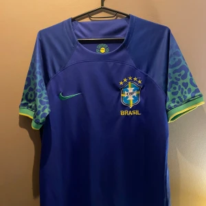 Blå Brasilien fotbollströja Nike - Snygg blå Brasilien fotbollströja från Nike med grönt Nike-märke och CBF-emblem på bröstet. Ärmarna har leopardmönster i blått och grönt samt gula detaljer vid ärmslut. Tillverkad i lätt och ventilerande material, perfekt för match eller träning.