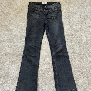 Bootcut jeans Abercrombie Kids svart - Snygga svarta bootcut jeans från Abercrombie Kids i low-rise modell. Jeansen har klassiska fickor fram och bak, bälteshällor och stängs med knapp och dragkedja. Perfekta för dig som gillar en avslappnad men trendig look.