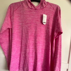 Rosa hoodie med huva i storlek L - Snygg rosa hoodie med melerad look och huva. Tröjan har långa ärmar och är tillverkad i ett mjukt och lätt material som passar perfekt för chill dagar eller träning. Enkel och stilren design utan tryck eller logga.