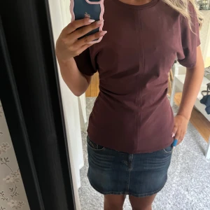 Vinröd t-shirt topp från Zara S - Säljer en vinröd t-shirt topp från Zara i storlek S. Modellen har korta ärmar, rund halsringning och markerad söm mitt fram. T-shirten är figurnära i midjan
