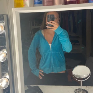 Blå velourjacka Juicy Couture  - Säljer en ikonisk blå velourjacka från Juicy Couture med dragkedja och huva. Baksidan har glittriga hjärtan och Juicy-logga i guld och strass. Jackan är långärmad och har två fickor framtill. Perfekt för en chill och trendig look.