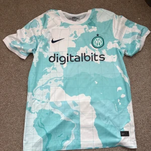 Inter Milan bortatröja 2022/23 Nike - Säljer en Inter Milan bortatröja från säsongen 2022/23. Tröjan är kortärmad och har ett unikt världskartemönster i ljusblått och vitt. Digitalbits och Lenovo-loggor samt Inter-emblem på bröstet. Tillverkad i lätt och ventilerande polyester.