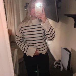 Vit och svart randig stickad tröja - Säljer en snygg vit stickad tröja med svarta ränder. Tröjan har en rund hals och långa ärmar med ribbade muddar💗