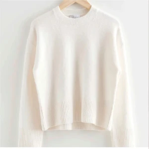 Vit stickad tröja med ribbade detaljer - Mysig vit stickad tröja med rund hals och breda ribbade muddar vid ärmslut och nederkant. Tröjan har en relaxed passform och är perfekt för lager-på-lager under kyliga dagar. Enkel och stilren design som funkar till allt.