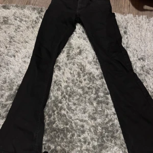 Svarta lågmidjade bootcut jeans från Gina Tricot - Svarta jeans i storlek 34. De är lågmidjade och bootcut. De har små hål nere vid benens slut eftersom jag trampat på byxorna när jag gått. (Det vita går bort)