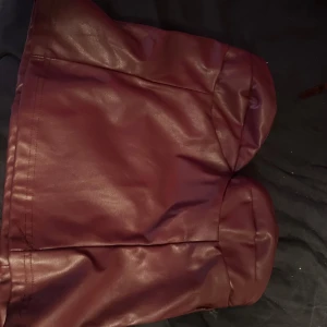 Vinröd skinn tubtopp med hjärtformad byst - Säljer en vinröd tubtopp i skinnimitation med hjärtformad byst. Toppen är axelbandslös och har en stilren, tight passform som ger en edgy vibe. Perfekt för dig som vill sticka ut med en cool och trendig look.