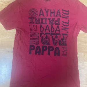 Röd t-shirt med tryck från Mywear Man - Röd t-shirt från Mywear Man Department 1987 i storlek S. T-shirten har coolt svart tryck med olika ord för pappa på framsidan. Klassisk passform med rund hals och korta ärmar. Perfekt för dig som gillar statement-plagg och vill sticka ut.