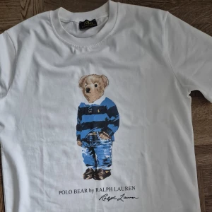 Polo ralph lauren T-shirt M - Säljer en helt ny polo ralph lauren T-shirt med den klassiska björnen på. Tröjan är aldrig använd men prislappen är tyvärr borta. Modellen är ikonisk och detaljerna med björnen gör den både stilren och unik. Skick 10/10