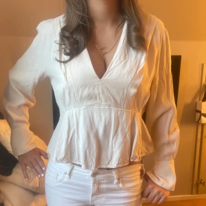 Vit blus med v-ringning - Säljer en stilren vit blus med v-ringning och långa ärmar. Blusen har en lätt utsvängd passform nedtill och markerad midja. Perfekt att matcha med jeans eller kjol för en clean look.