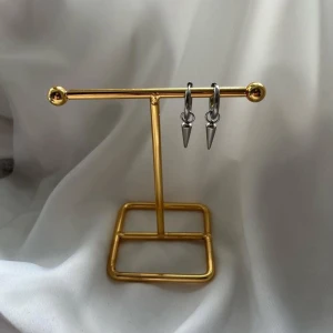 Silvriga örhängen med spike-detalj - Säljer ett par coola silvriga örhängen med små spike-hängen. De har en minimalistisk och edgy design som passar perfekt för dig som gillar att sticka ut. Örhängena är i metall och har en enkel ring med en spetsig detalj som hänger ner.