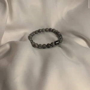 Grått pärlarmband med marmormönster - Stilrent armband med runda grå pärlor i marmormönster och en metallisk detalj. Elastiskt band gör det enkelt att ta på och av. Perfekt accessoar för att lyfta din outfit med en cool touch.