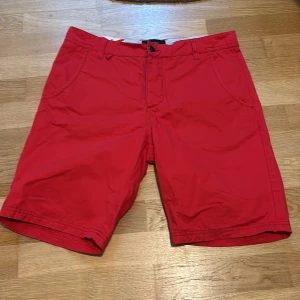 Röda shorts från Bondelid - Snygga röda shorts från Bondelid med klassisk passform och praktiska fickor fram. Perfekta för varma dagar och har bälteshällor samt knapp och dragkedja i midjan. Tillverkade i mjuk bomull som känns skön mot huden.