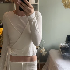 Vit omlottopp från 157, XS - Superfin vit omlottopp från 157 i mjuk bomull. Långärmad modell med knyt i sidan och rund halsringning. Perfekt att styla med jeans eller kjol för en clean och fräsch look. Sitter snyggt och är riktigt bekväm!