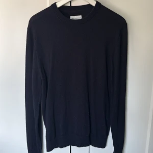 Svart merinoullströja These Glory Days - Klassisk svart rundhalsad tröja från These Glory Days i mjuk merinoull. Enkel och stilren design med ribbade muddar vid ärmslut och nederkant. Perfekt för lager-på-lager och funkar året runt för en clean look. Köpt på VOLT