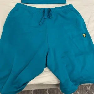 Shorts XL  tishirt M - Turkosa shorts och tishirt från Lyle & Scott med elastisk midja och snörning. Klassisk gul logga broderad på vänster ben. Sköna och avslappnade, perfekta för sommardagar. Tillverkade i mjuk bomull för maximal komfort.