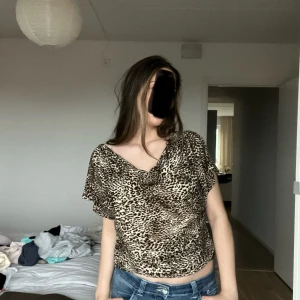 Leopardmönstrad omlottopp med drapering - Säljer en leopardmönstrad omlottopp med draperad front och korta ärmar. Toppen har en lös passform och är tillverkad i ett mjukt, stretchigt syntetmaterial. Funkar som storlek M/L och kan användas i olika former 🤎 Perfekt skick 