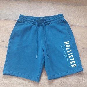Blå Hollister shorts med snörning XS - Mörkblå shorts från Hollister i mjuk bomull med snörning i midjan och tryckt logga längs ena benet. Modellen har normal passform, sidofickor och en bakficka. Perfekta för chill dagar på sommaren.