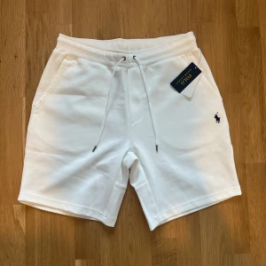Vita shorts från Polo Ralph Lauren - Snygga vita shorts från Polo Ralph Lauren med klassisk logga broderad på vänster ben. Modellen har snörning i midjan, två sidofickor och en bakficka. Mjukt bomullsmaterial som är perfekt för sommaren. Enkel och clean design som passar till allt.