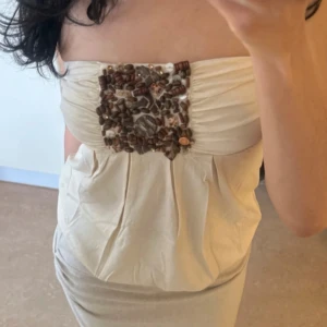 Champagnefärgad tubtopp  från MET - Superfin tubtopp från MET i skimrande champagnefärg. Toppen har en unik detalj med handsydda pärlor och stenar i brunt och beige framtill. Sitter snyggt med lätt rynk vid bysten och har en luftig passform. Perfekt för dig som vill sticka ut med något annorlunda💘💘 ord pris 987kr!! Ny