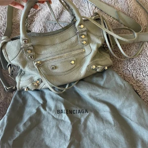 Balenciaga City Mini  - Säljer en ljusgrå handväska från Balenciaga i skinn med silverfärgade metalldetaljer och dragkedja framtill. Väskan har både handtag och axelrem, dustbag och kasse medkommer !🥰🩷✨köptes på Balenciaga i Milano. Bara att höra av er för mer detaljbilder eller frågor 🫶🏼