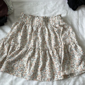 Blommig volangkjol från SHEIN - Supersöt kort kjol från SHEIN med blommigt mönster i beige, orange och grått. Kjolen har volanger och bred resår i midjan för en bekväm passform. Perfekt för dig som gillar en romantisk och trendig stil.