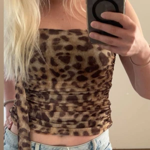 Leopardmönstrad croppad tubtopp - Säljer en croppad tubtopp med leopardmönster och knytband i sidan. Toppen har en åtsittande passform och är perfekt för att sticka ut. Materialet är stretchigt och mjukt.