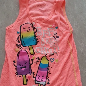 Topp - Säljer en söt orange/korall ribbad linnetopp med färgglada glassar och texten 'Be rare & so chill!' framtill. Toppen har ärmlös design och lekfulla detaljer i blått, gult och lila. Perfekt för varma dagar!