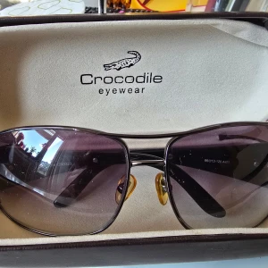 Guldiga solglasögon från Love Moschino - Snygga solglasögon från Love Moschino med tunn guldfärgad metallbåge och spegelglas i guldton. Trendig design med dubbla bryggor och klassisk form. Perfekt accessoar för att lyfta din stil.