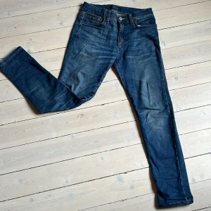 Blå jeans från Polo Ralph Lauren - Säljer ett par blå slim jeans från Polo Ralph Lauren, modell The Eldridge. Klassisk femficksdesign med snygga kontrastsömmar och läderpatch bak i midjan. Perfekta för dig som  vill ge din stil en extra touch
