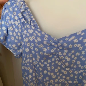 Blå blommig klänning från Holly & Whyte - Supersöt blå klänning med vita blommor från Holly & Whyte. Klänningen går att ha både över och nedanför axlarna. Perfekt för sommarens alla tillfällen! Materialet känns lätt och luftigt. Kontakta för frågor och prisförslag!