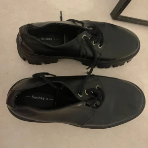 Chunky svarta skor från Bershka - Chunky svarta skor från Bershka med grov sula och snörning. Skorna har rund tå och är gjorda i syntetmaterial med en stilren look. Perfekta för dig som gillar en edgy och trendig stil.