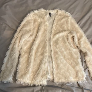 Beige pälsjacka från H&M Divided - Säljer en fusk pälsjacka från H&M Divided. Jackan har lång ärm och öppen front utan knäppning. Perfekt för dig som vill ha en trendig och mysig look.