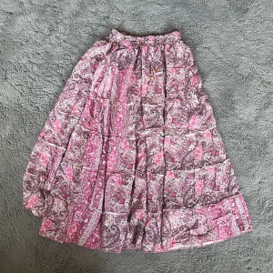 Rosa mönstrad långkjol med volang - Supersöt långkjol i rosa och lila toner med blommigt och paisleyinspirerat mönster. Kjolen har resår i midjan och flera volanglager som ger en flowy och bohemisk känsla. Perfekt för dig som gillar färg och mönster! ( Jag som är en 174 så slutar kjolen vid fotknuten o lite högre upp), Storleken är M/L