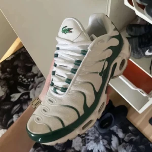 Nike Air Max Plus Tn sneakers i vitt och grönt - Nike Air Max Plus Tn sneakers i vitt med gröna detaljer och klassisk Tn-logo bak. Skorna har snörning, rund tå och platt sula. Snyggt vågmönster på ovandelen och meshmaterial för bra andningsförmåga. Perfekta för dig som gillar sportig stil.