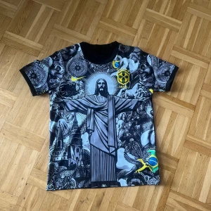 Brasil Neymar Jr 10 Nike fotbollströja - Unik Brasilien fotbollströja från Nike med Neymar Jr och nummer 10 på ryggen. Tröjan har svart bas med detaljerade grafiska tryck i grått och vitt, gula och blå accenter samt CBF-emblem på bröstet. Tillverkad i lätt funktionsmaterial och har korta ärmar.