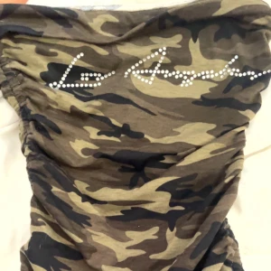 Camo kortklänning från SHEIN XS - Snygg camouflagemönstrad kortklänning från SHEIN i storlek XS. Klänningen har coola snörningsdetaljer på sidorna och text i strass framtill. Mjukt material som känns skönt mot huden och passar perfekt för dig som vill sticka ut.