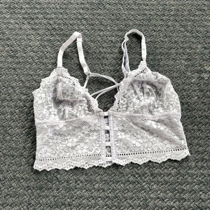 Vit spetsig bralette topp - Superfin vit spetsig bralette topp med smala axelband och dekorativa banddetaljer framtill. Toppens spets har blommigt mönster och kanten är vågig för extra söt vibe. Perfekt att styla under en öppen skjorta eller till höga jeans. Tryck ej köp nu