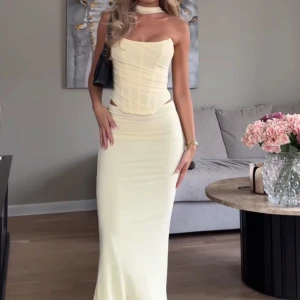 Ljusgul  set topp och kjol  - Säljer en elegant ljusgul långklänning med figurnära passform och omlott-detalj i midjan. Klänningen har smala axelband och en mjuk, feminin siluett. Perfekt för sommarens tillfällen. ALDRIG ANVÄND